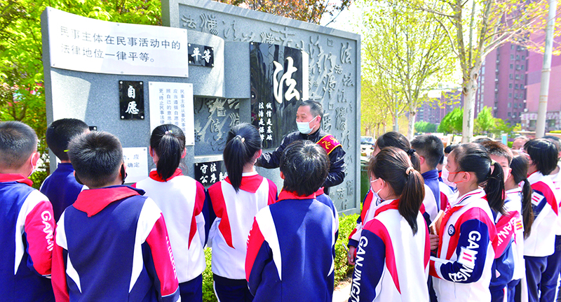 頭題圖,普法志愿者在憲法墻前給學生們普及法律知識。